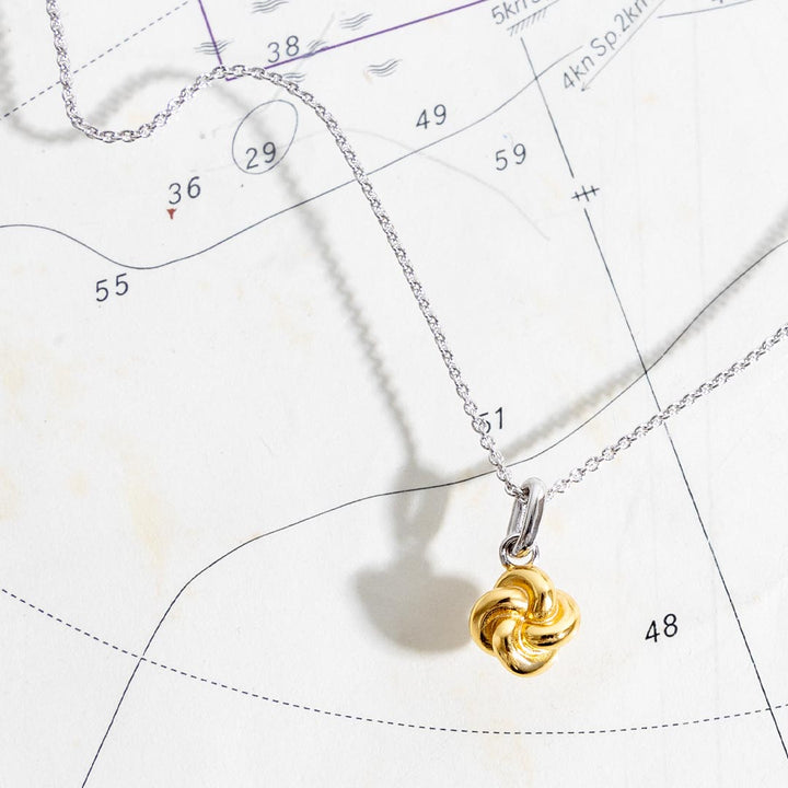 Gold knot pendant on a silver chain against a star map background