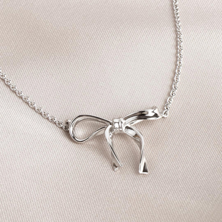Silver bow-shaped necklace on a light beige fabric background