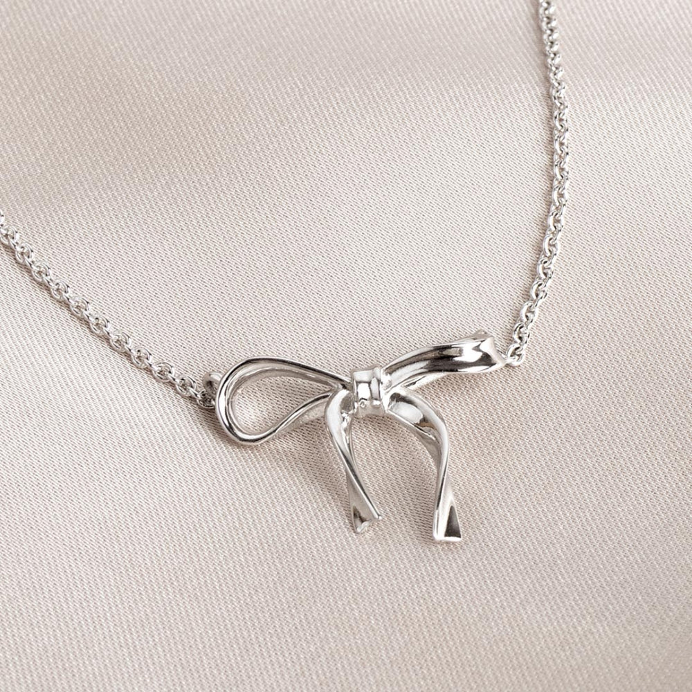 Silver bow-shaped necklace on a light beige fabric background