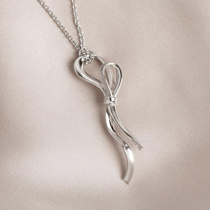 Silver bow-shaped pendant on a chain against a beige background