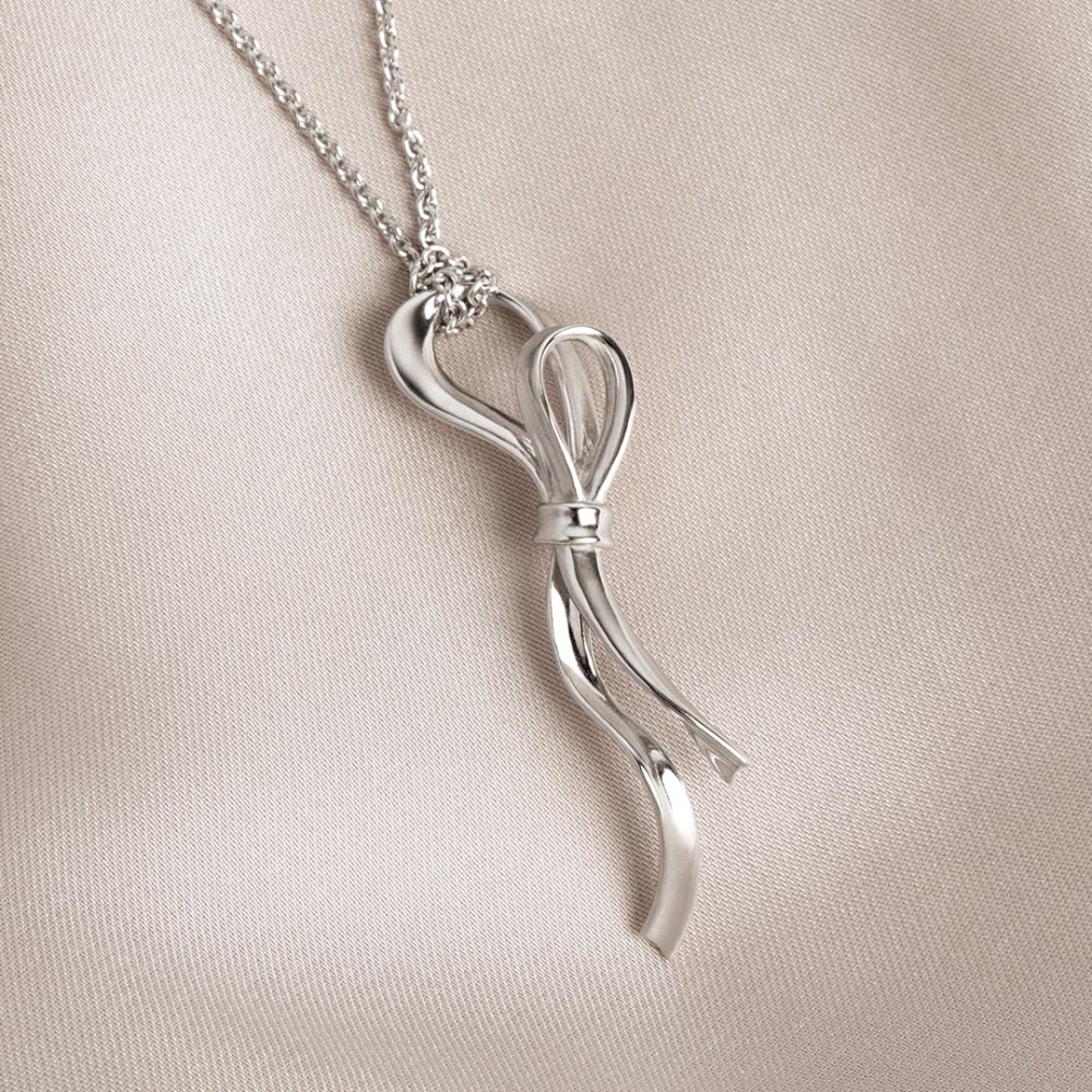 Silver bow-shaped pendant on a chain against a beige background