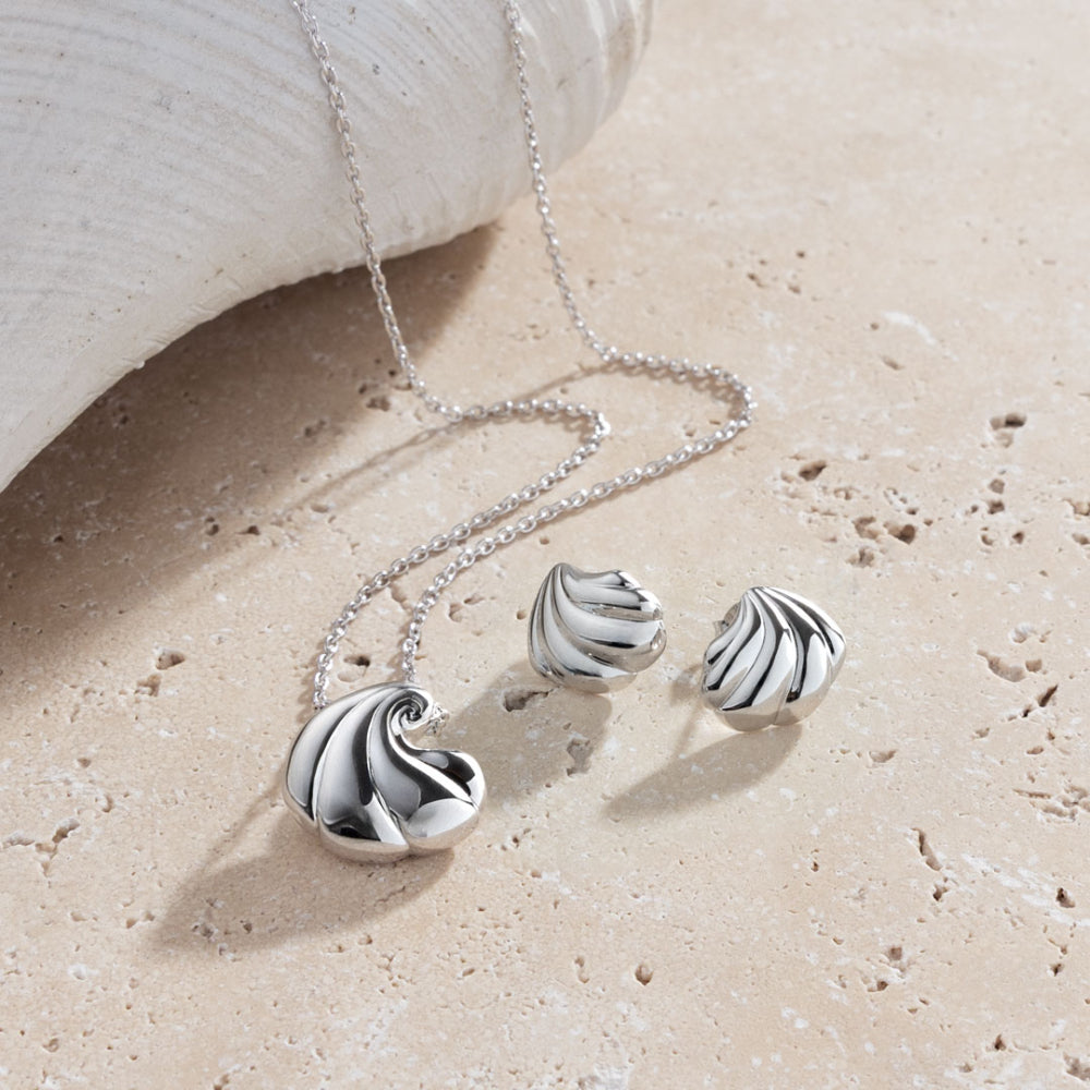 Silver wave necklace and earrings on a sandy surface