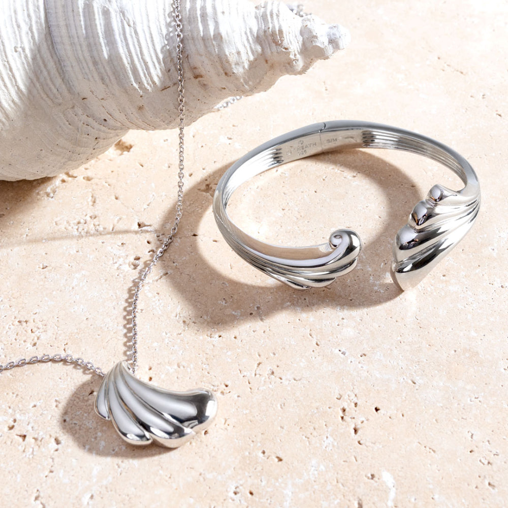 Silver bracelet and necklace with wave design on a sandy surface