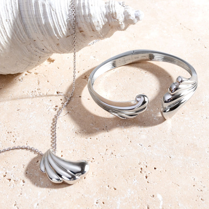 Silver bracelet and necklace with wave design on a sandy surface
