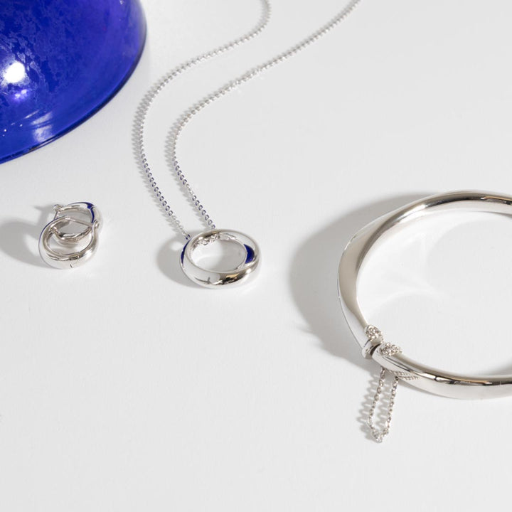 Silver jewelry set including necklace, earrings, and bracelet on a white background