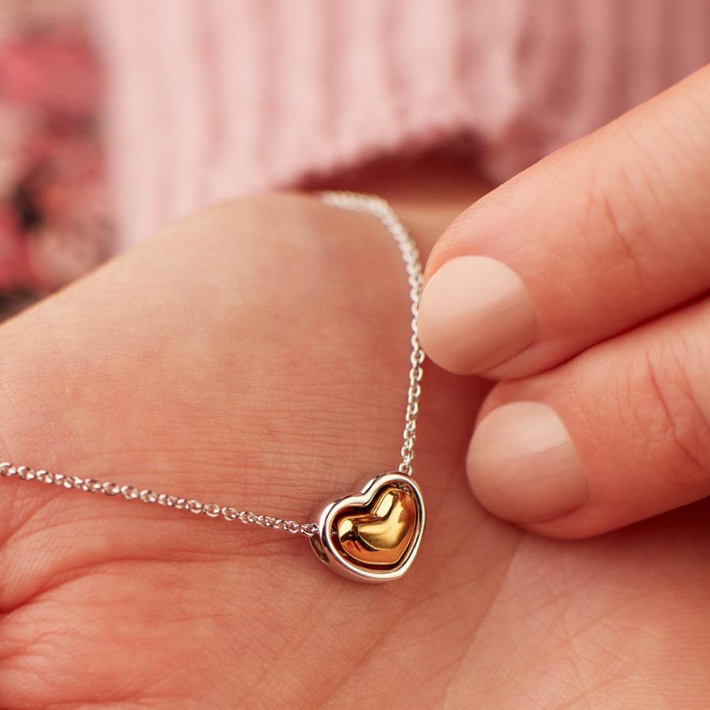 Gold heart-shaped pendant on a silver chain held between fingers