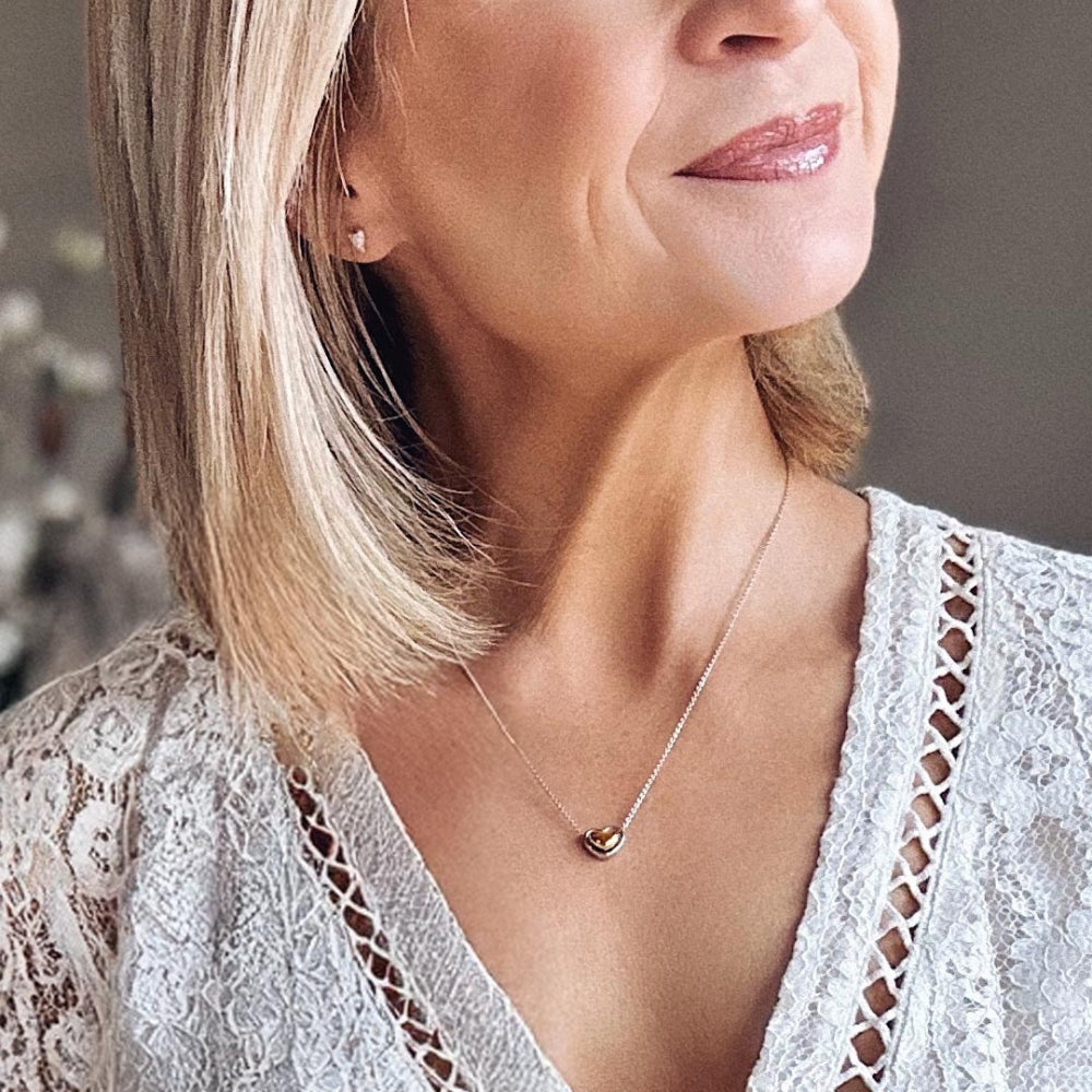 Woman wearing a delicate necklace with a heart pendant, close-up of her neck and shoulders.