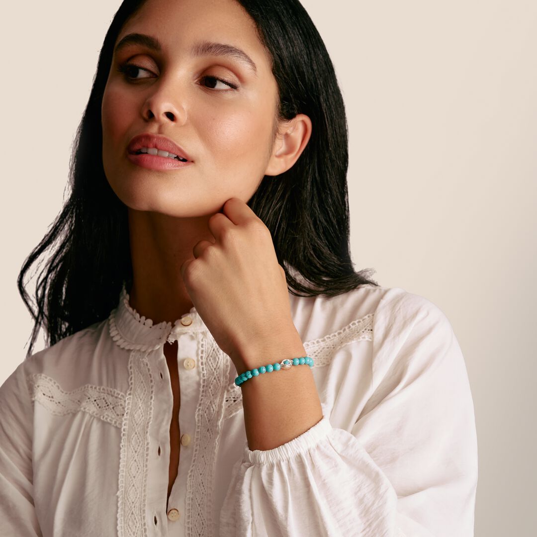 Woman wearing a white blouse and turquoise bracelet on a beige background