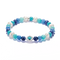 A beaded stretch bracelet featuring a mix of white pearls, light and dark blue beads, and turquoise-blue marbled beads, accented by a silver-tone evil eye charm with a turquoise center, shown on a clean white background.