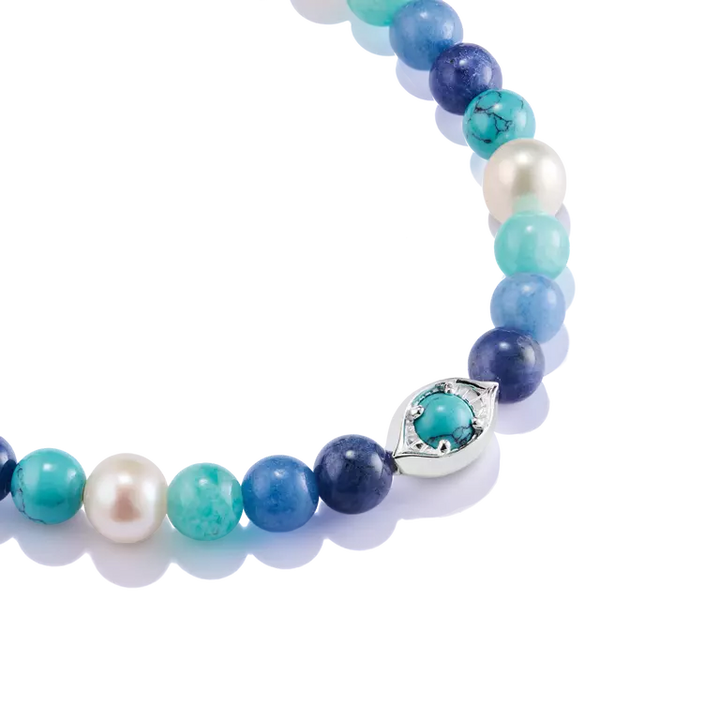 A close-up of a beaded necklace featuring round turquoise-blue and white pearls, accented by a silver-toned evil eye charm with a turquoise center, set against a clean white background.