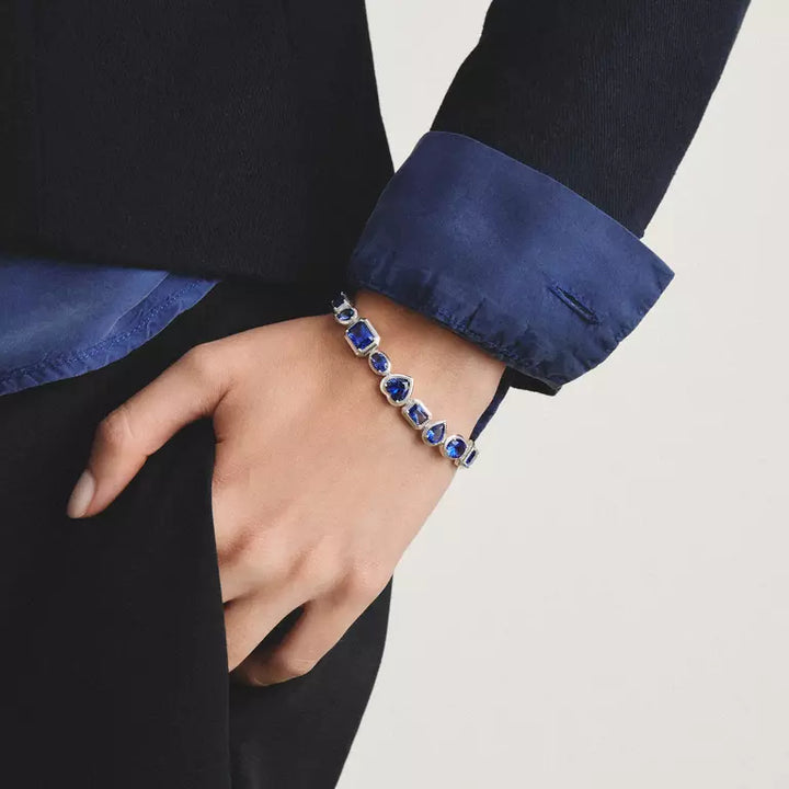 A close-up of a person's hand wearing a silver-toned bracelet with oval-cut deep blue gemstones, styled with a dark blazer and a blue shirt cuff.