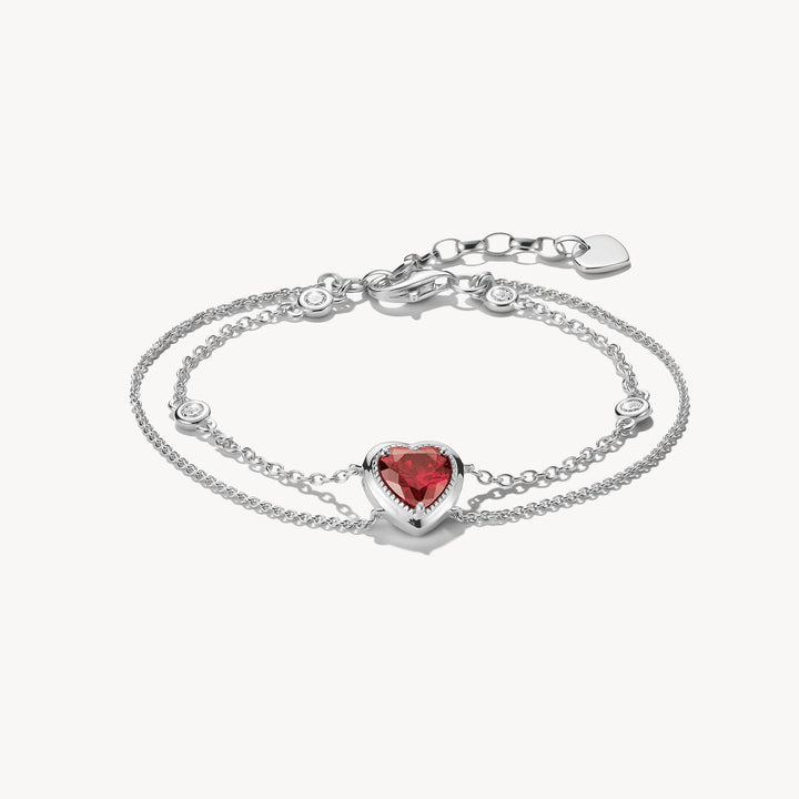 Silver bracelet with a heart-shaped red gemstone on a white background
