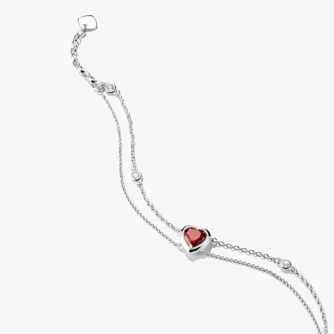 Silver bracelet with a heart-shaped red gemstone on a white background