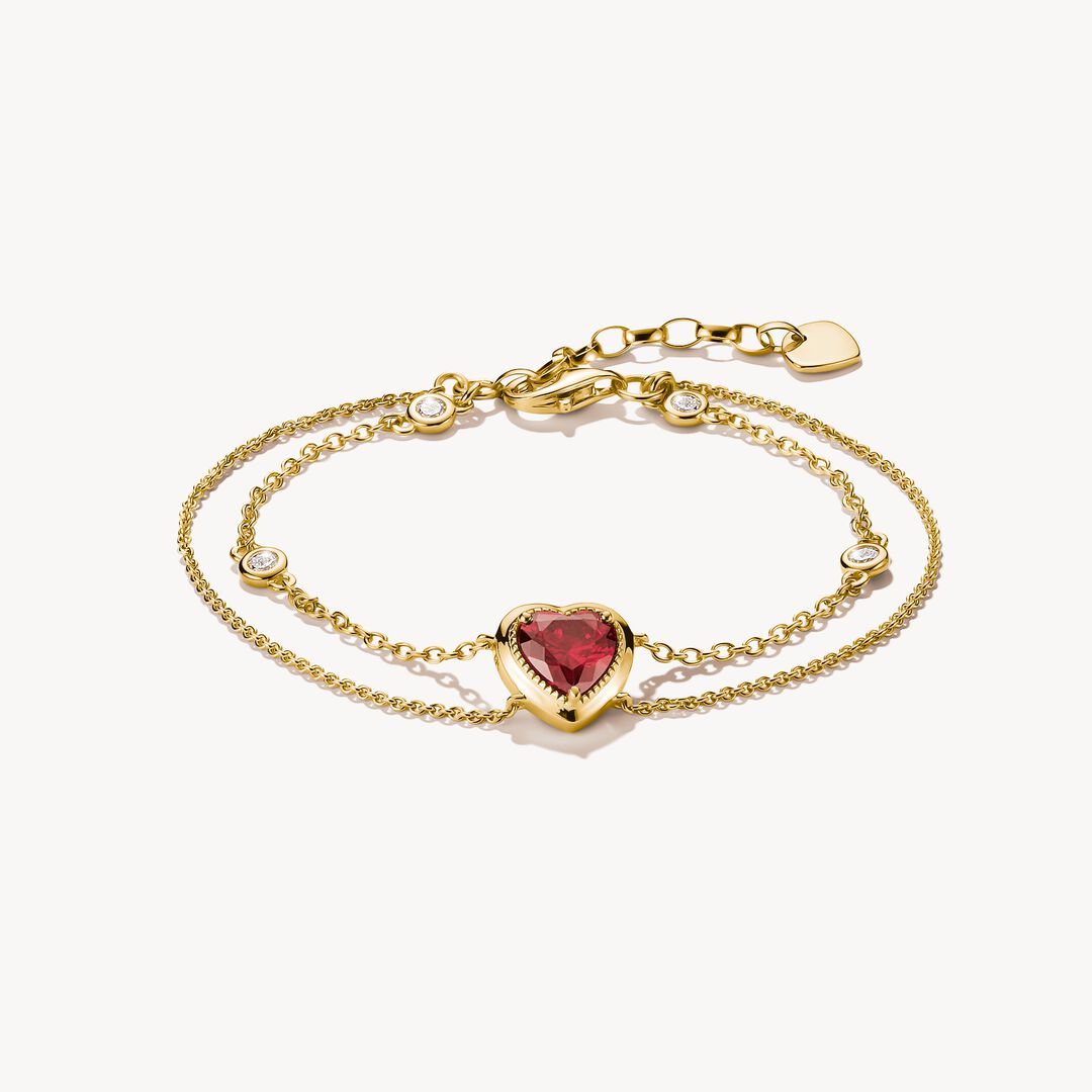 Gold bracelet with heart-shaped red gemstone on a white background