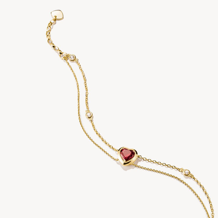 Gold bracelet with a heart-shaped red gemstone on a white background
