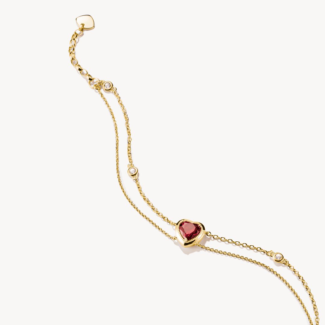 Gold bracelet with heart-shaped red gemstone on a white background