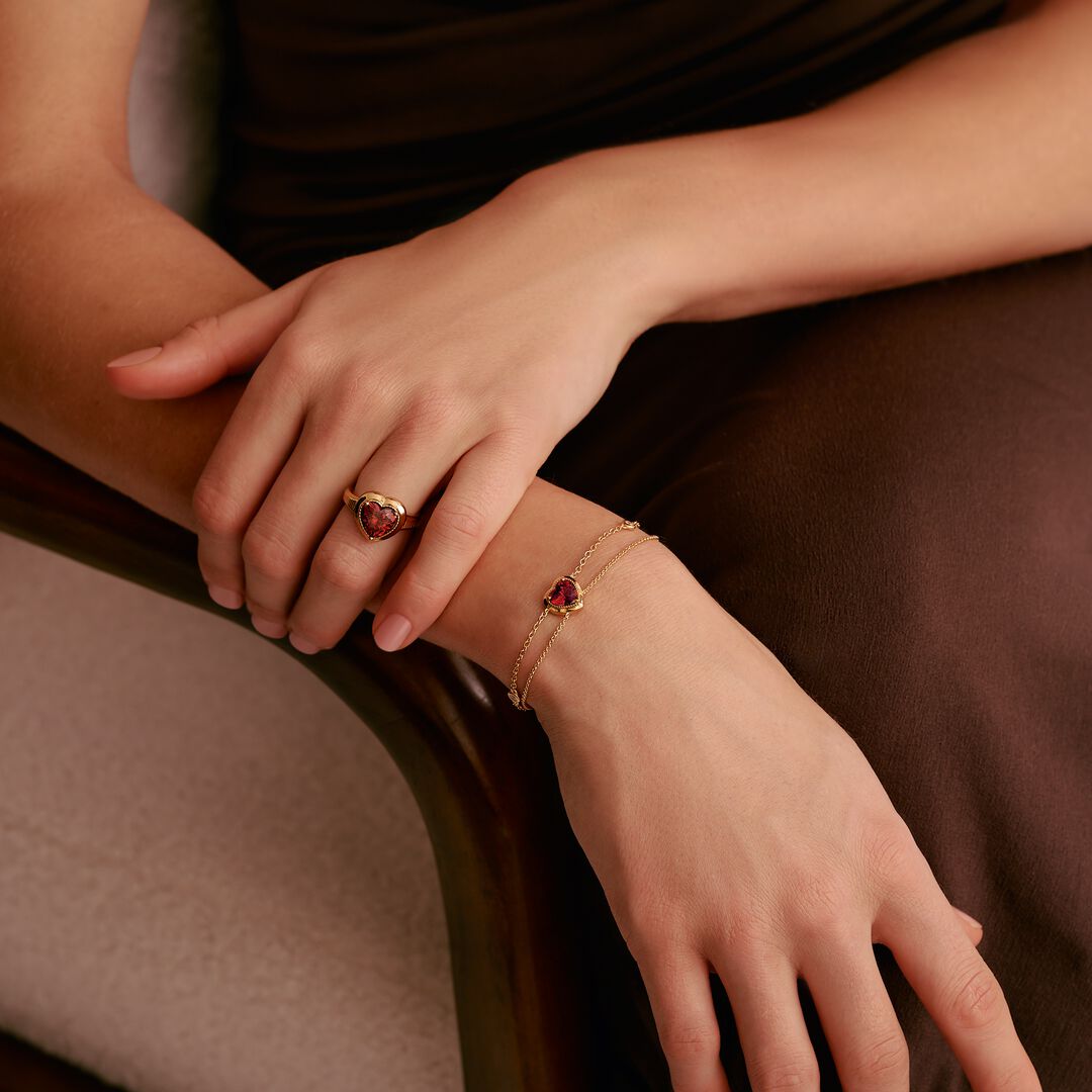Close-up of hands wearing gold rings and bracelets with red gemstones on a brown background
