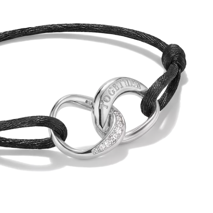 A silver interlocking rings bracelet with a black cord, featuring a pavé-set clear crystal accent and the word 'TOGETHER' engraved on one ring, shown on a white background.