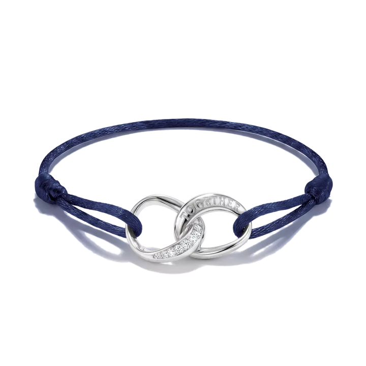A navy blue cord bracelet with a polished silver infinity-style centerpiece featuring a pavé-set clear stone and the engraved word 'LOVE' on one loop, shown on a white background.