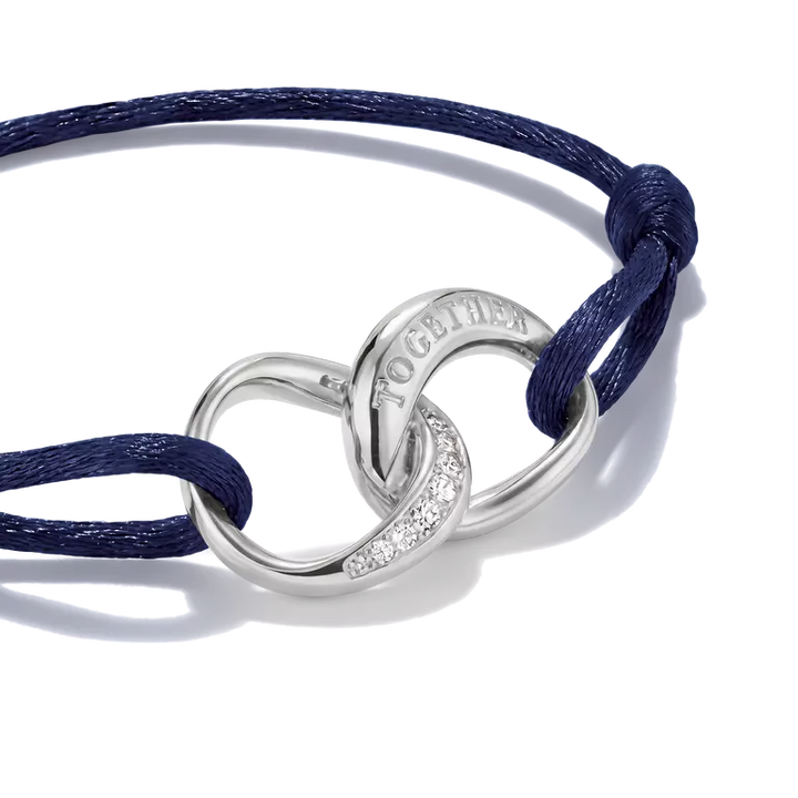 A navy blue cord bracelet with a polished silver interlocking rings centerpiece, one engraved with 'TOGETHER' and the other accented with small clear crystals, shown on a white background.