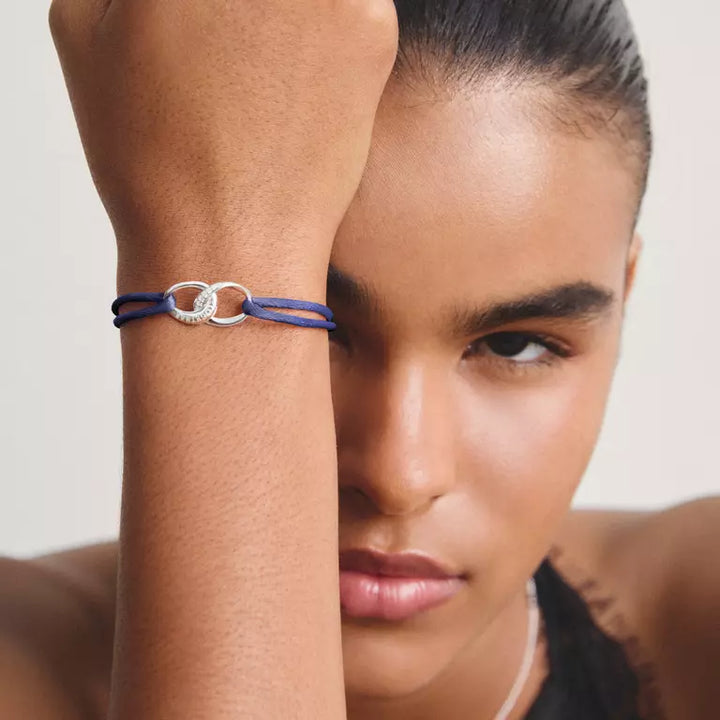 A close-up lifestyle shot of a model wearing a delicate bracelet on her wrist. The bracelet consists of a dark blue cord wrapped around a polished silver-tone double-ring charm.