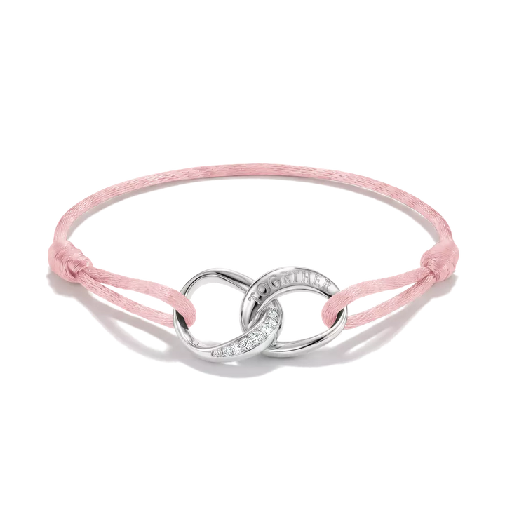 A delicate pink cord bracelet featuring a polished silver infinity symbol centerpiece with a small pavé diamond accent and the engraved word 'LOVE'.