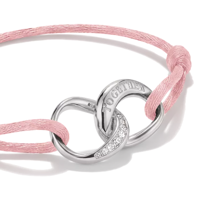 A silver-toned double-ring charm bracelet with a pink woven cord and small clear stones, featuring the engraved word 'TOGETHER' on one ring, shown on a white background.