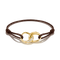 A brown cord bracelet featuring an interlocking gold infinity-style charm with a pavé diamond accent and the brand name 'Chap-Guillaume' engraved on one loop, shown on a white background.