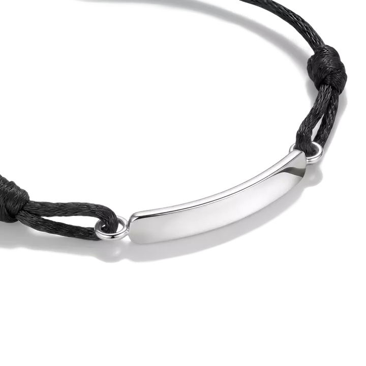 A silver curved bar nameplate bracelet on a black adjustable cord, shown on a clean white background.