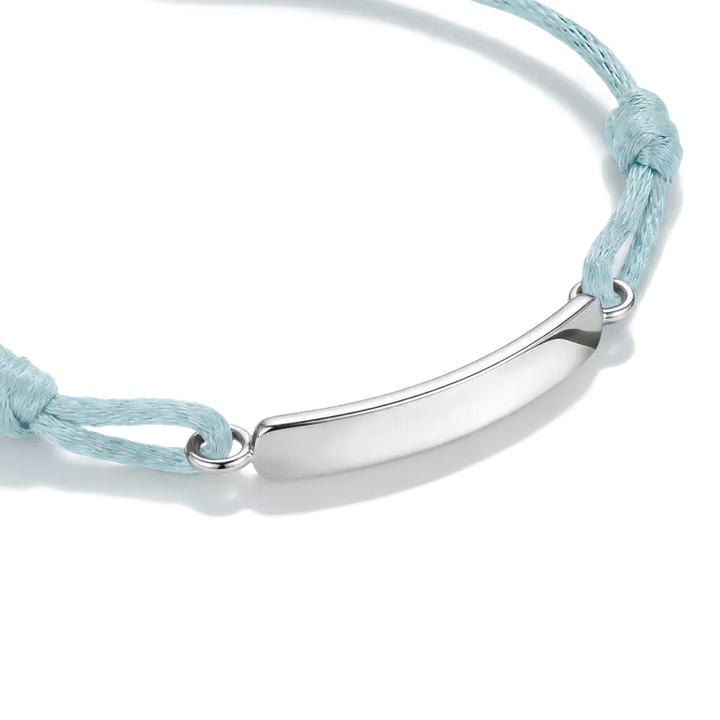 A silver-toned curved bar nameplate bracelet on a light blue cord, shown on a clean white background.