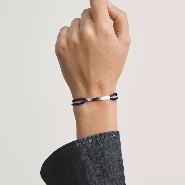 A silver-toned metal bracelet with two dark blue oval links, worn on a person's wrist against a light gray background.