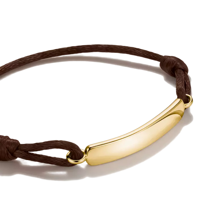A brown cord bracelet with a polished gold ID bar and matching gold eyelets, shown on a clean white background.