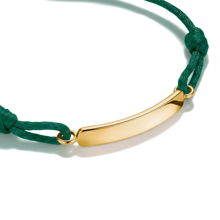 A close-up of a gold-plated curved ID bar bracelet on a dark green cord, shown against a clean white background.