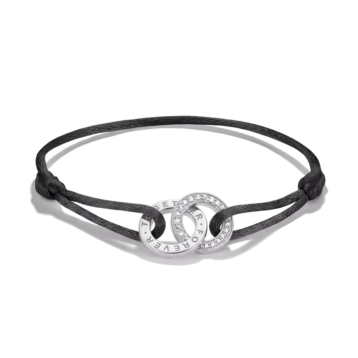A black cord bracelet with two interlocking silver rings, one of which is paved with small clear stones and features the text 'I WILL NEVER FORGET YOU' engraved on the other, shown on a white background.