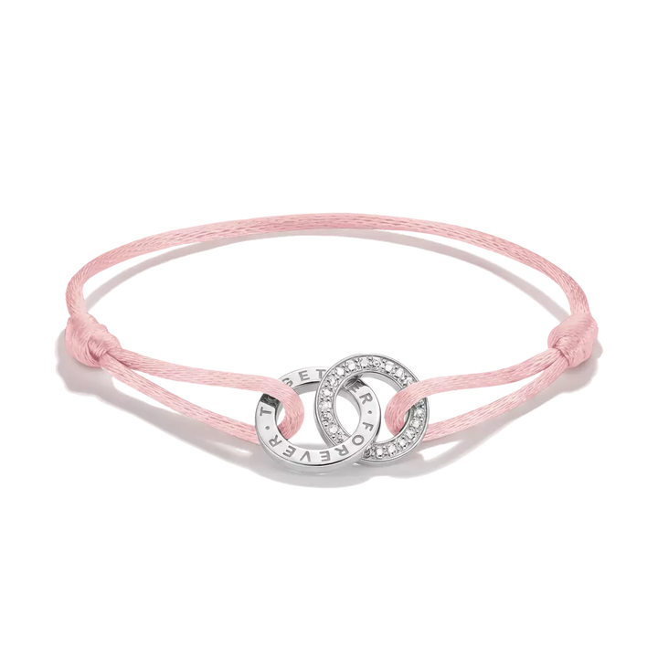 A delicate pink cord bracelet featuring two interlocking silver rings, one of which is adorned with small clear crystals and the other engraved with the word 'FOREVER'.