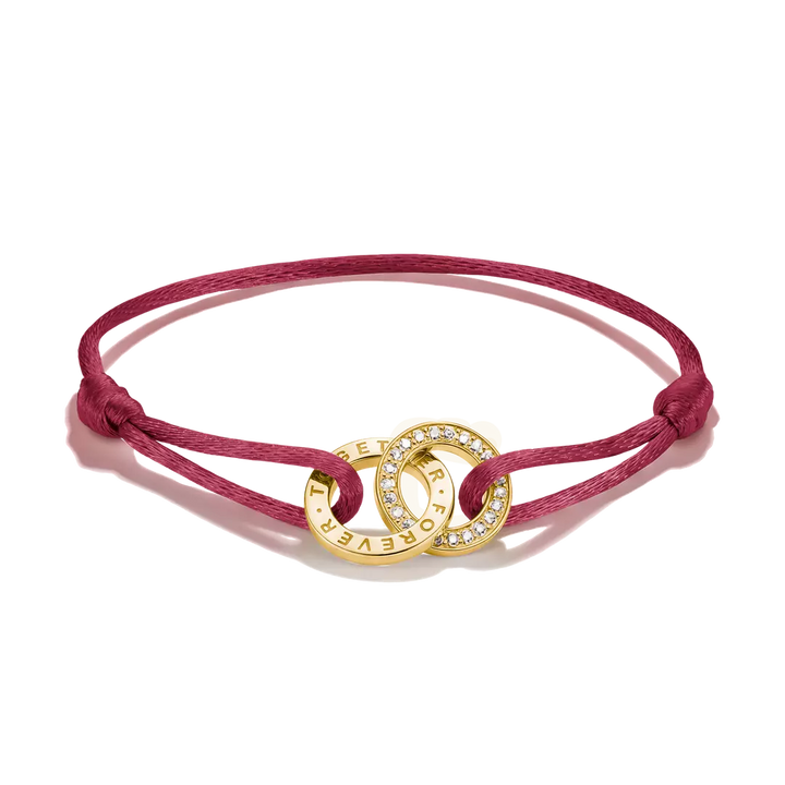 A magenta pink cord bracelet with a gold-toned interlocking rings centerpiece, one ring set with small clear crystals and the other engraved with 'I LOVE YOU' and 'FOREVER'.