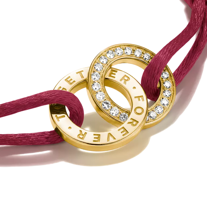 A magenta pink cord bracelet with a gold-toned interlocking rings centerpiece, one ring set with small clear crystals and the other engraved with 'I LOVE YOU' and 'FOREVER'.