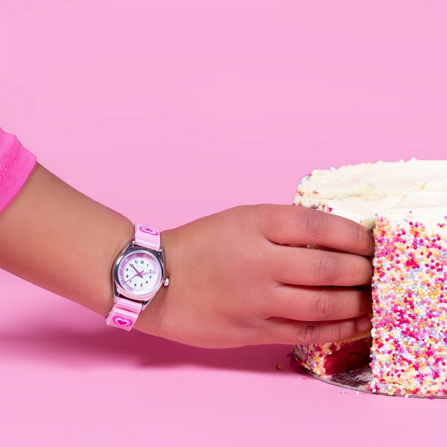 Child's hand wearing a pink watch on a pink background with a cake.