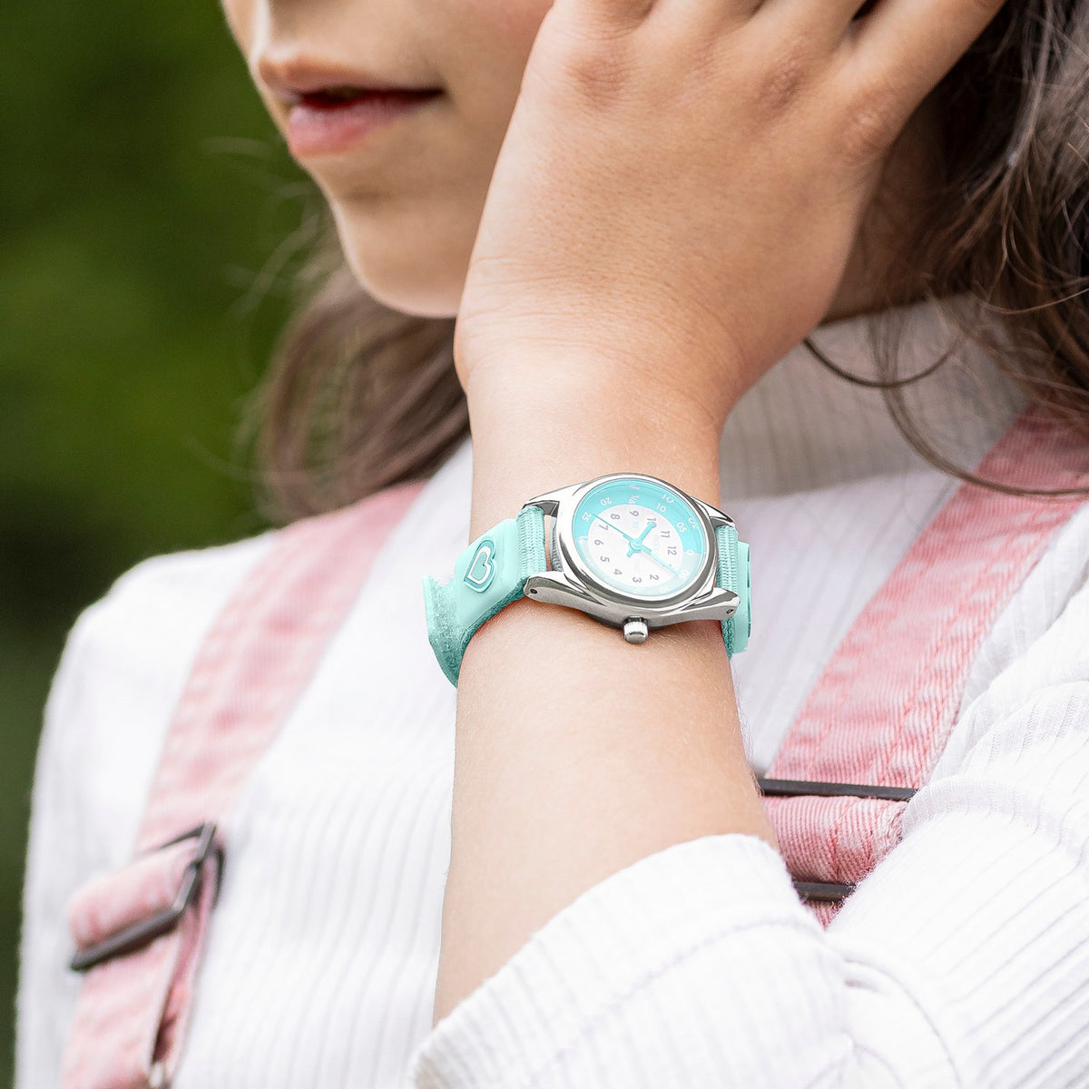 Person wearing a turquoise watch with a blurred green background