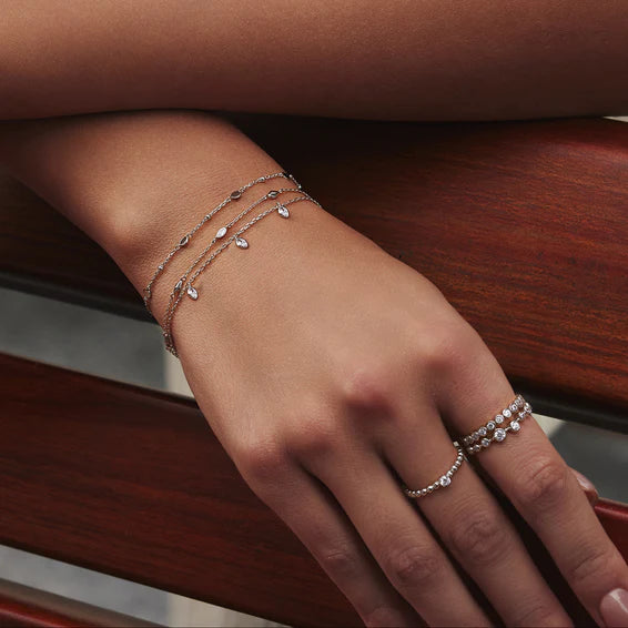 Hand wearing multiple silver bracelets and a ring on a wooden surface