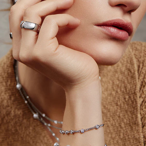 Close-up of a woman's hand wearing a silver ring and bracelet, with a blurred background.