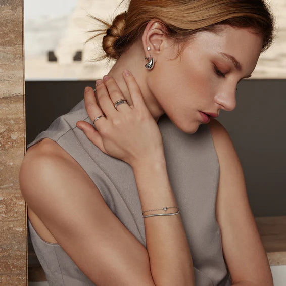 Woman wearing jewelry including earrings, ring, and bracelet in a neutral setting.