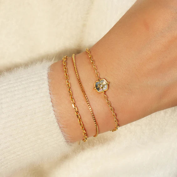 Gold bracelet with a hexagonal charm on a wrist against a soft beige background