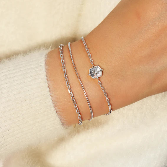 Two silver bracelets on a wrist against a beige background