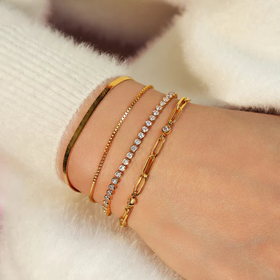 Close-up of a wrist wearing multiple gold and silver bracelets on a soft white background