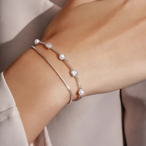 Silver bracelet with pearls on a wrist against a neutral background