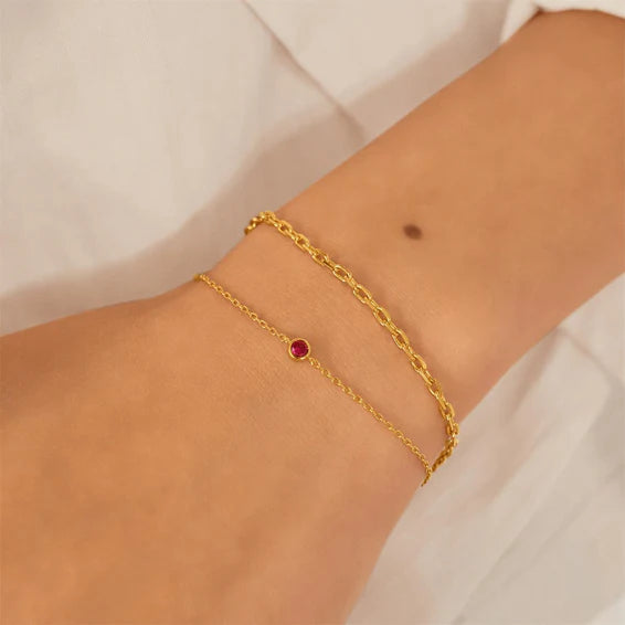Gold anklet with a red gemstone on a person's ankle against a white background