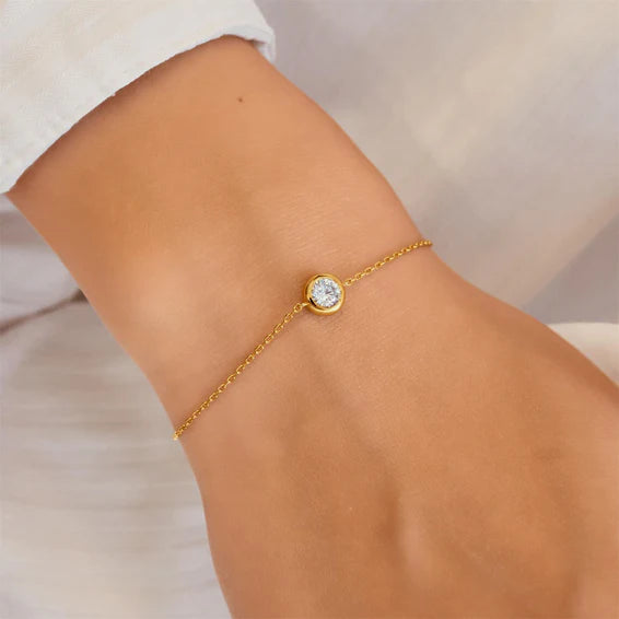 Gold bracelet with a diamond on a wrist against a neutral background