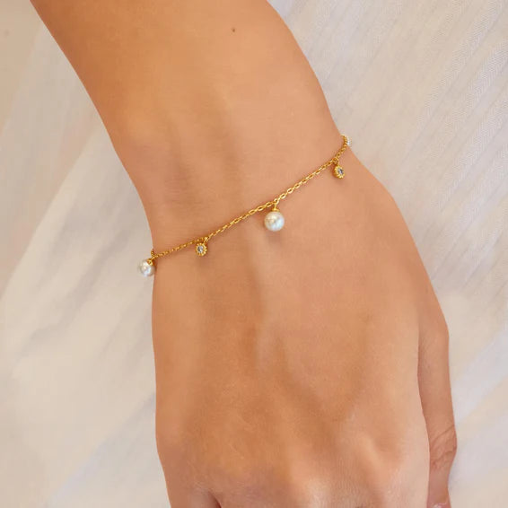 Gold anklet with pearls on a person's ankle against a neutral background