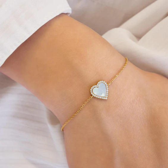 Gold bracelet with a heart-shaped charm on a wrist against a neutral background